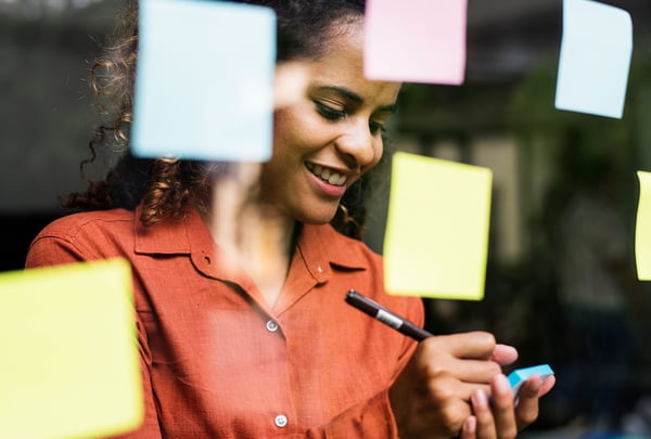 Person writing on sticky notes on glass