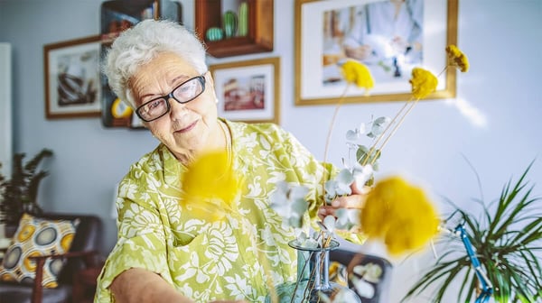 An elderly lady tending to some cut flowers in a vase