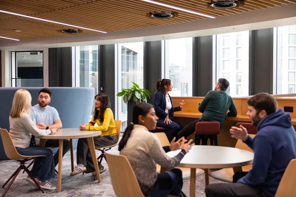 Employees engaged in conversation while seated at small round tables and on counter stools in L&G's Cardiff office.