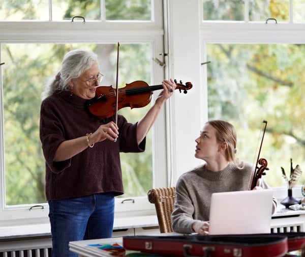 An older lady teaching a younger girl the violin, while standing up playing music