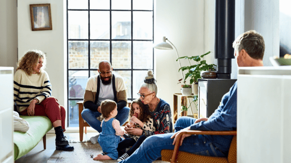 A family sat in a living room, with a grandmother playing with 2 children on the floor