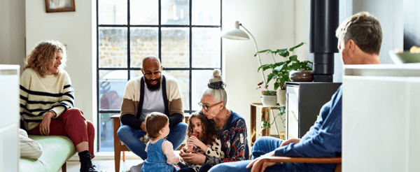 A family sat in a living room, with a grandmother playing with 2 children on the floor