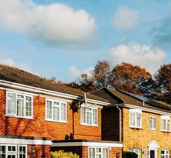 A close up of 2 brick semi-detached houses and their roofs, with clouds in the sky and trees