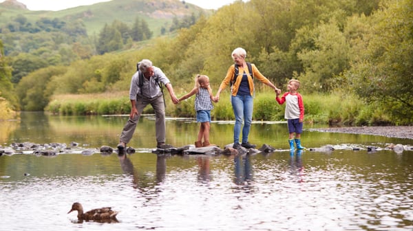 Grandparents with their 2 grandchildren, walking along a log on a river, holding hands