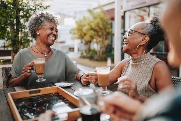 Two older ladies laughing together while sat at a table with lattes