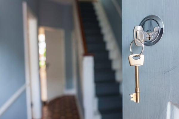 A close up view of a key in a open door, showing the hallway and stairs inside