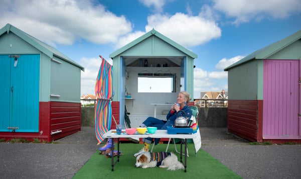 Woman in front of beach huts drinking coffee