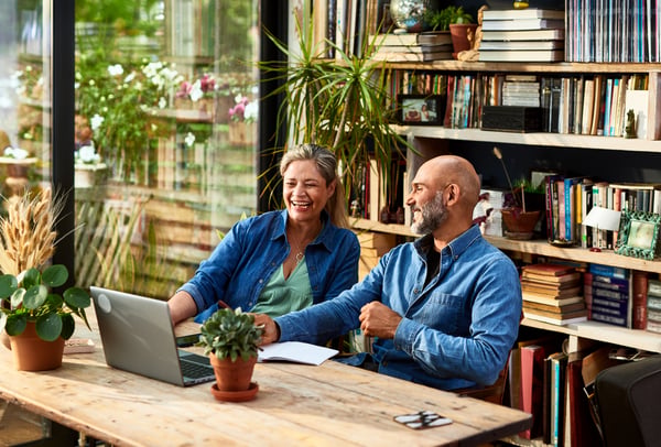 Couple sitting at table laughing while looking at a laptop