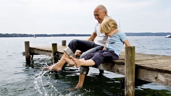 Grandfather and grandson splashing feet in the water on a jetty