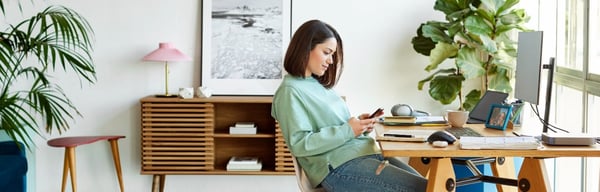 Image of a young woman sat at desk looking at mobile phone