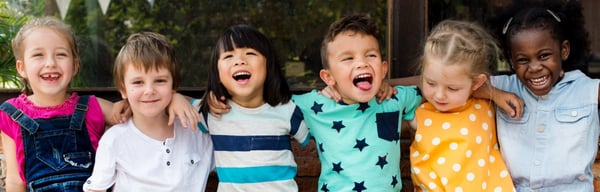 Young children sitting on a bench smiling and laughing
