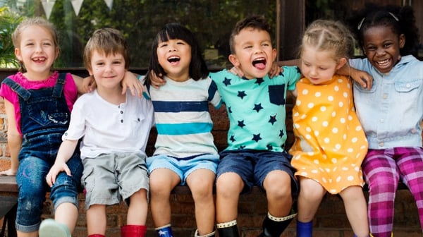 Young children sitting on a bench smiling and laughing