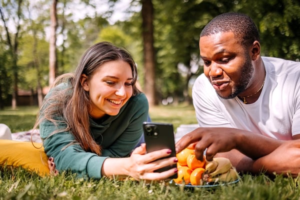 Two people viewing a mobile phone during a picnic