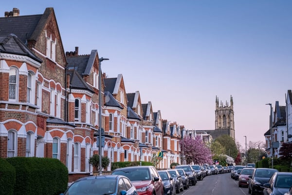 A residential street with Victorian terraced houses, parked cars and a church at the end of the road