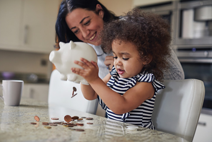 Toddler and Mum smiling and looking at a piggybank