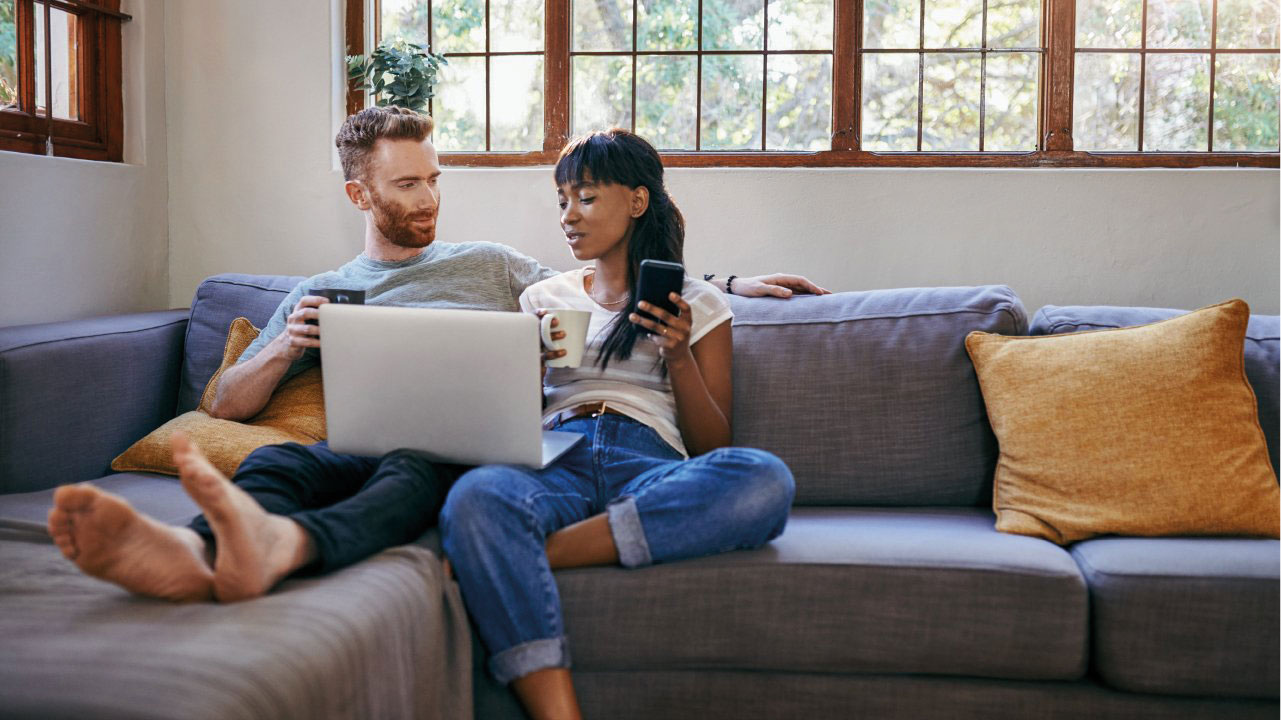 Couple on sofa looking at laptop and phone