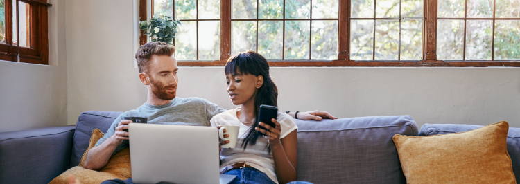 Couple on sofa looking at laptop and phone