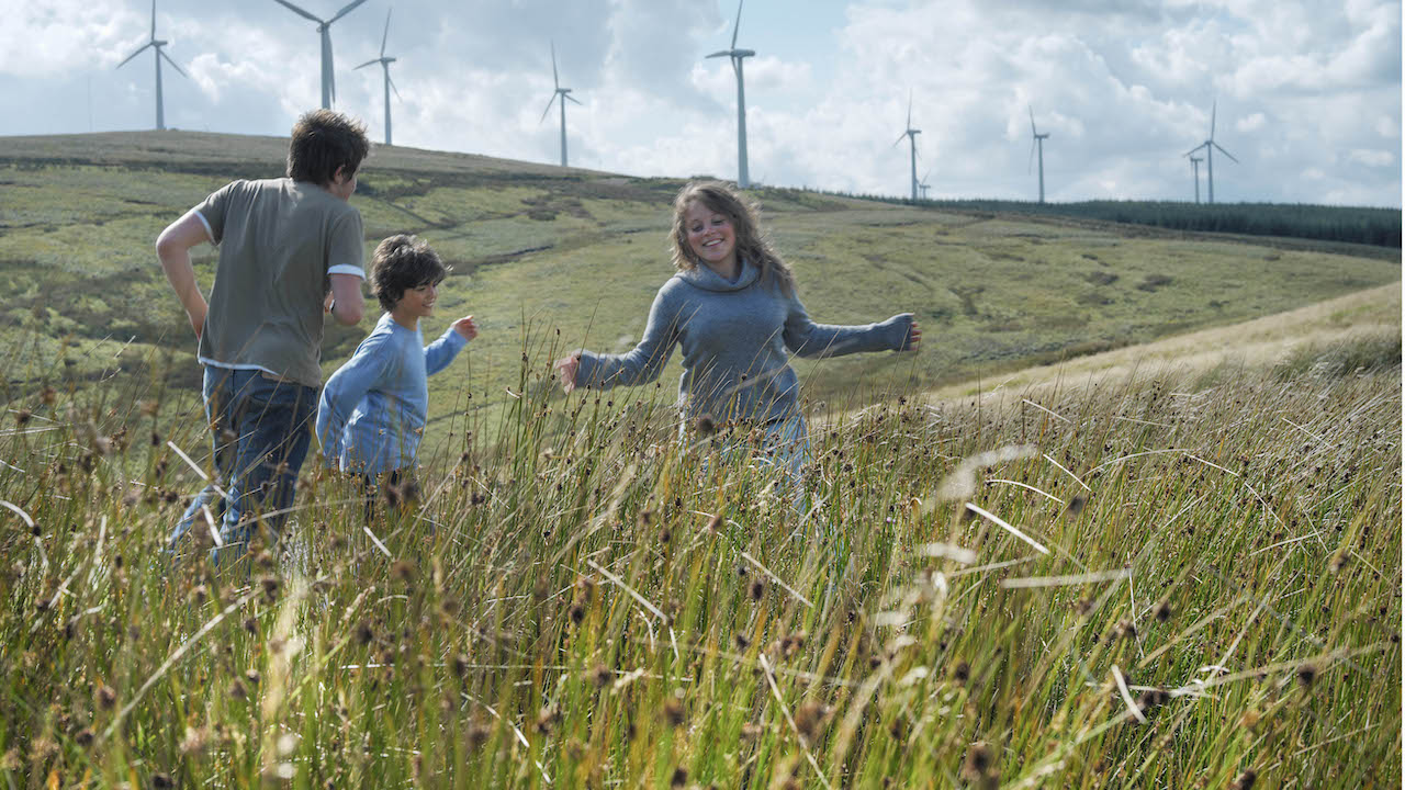 Happy young family in a field with windfarms
