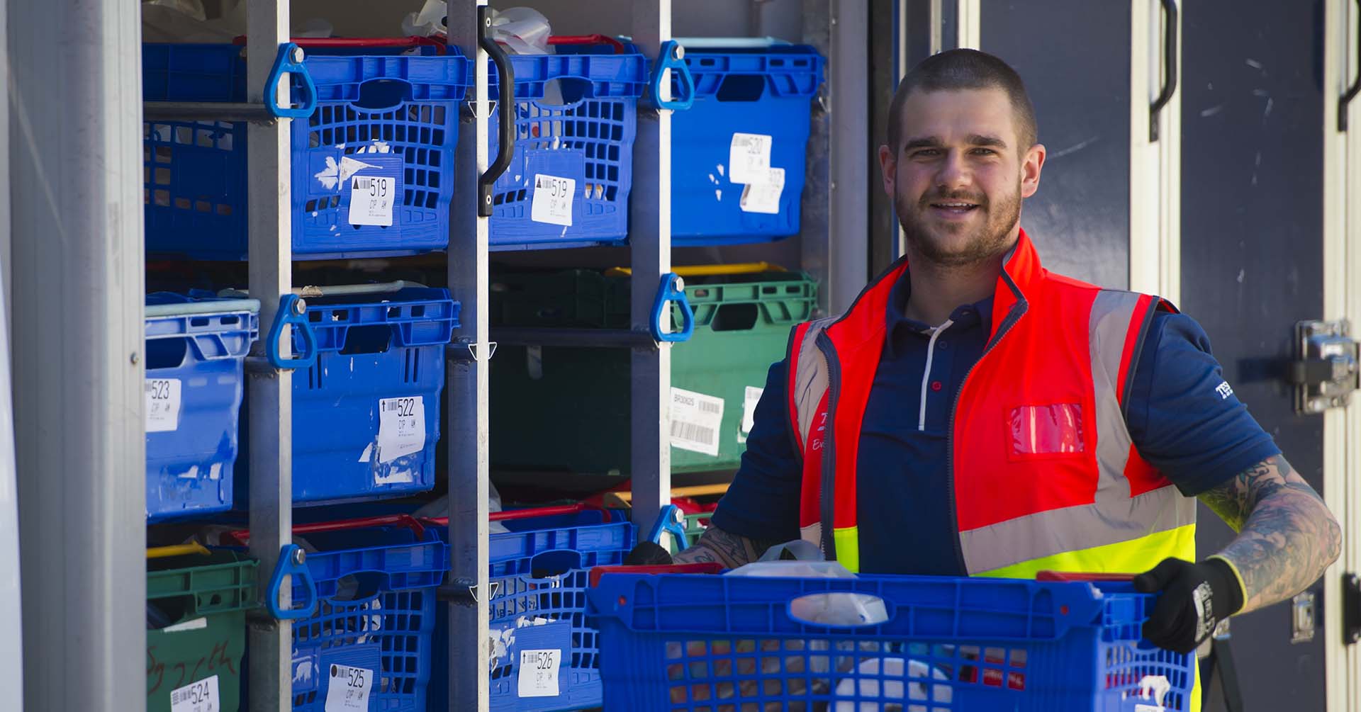 Smiling Tesco driver carrying box of groceries