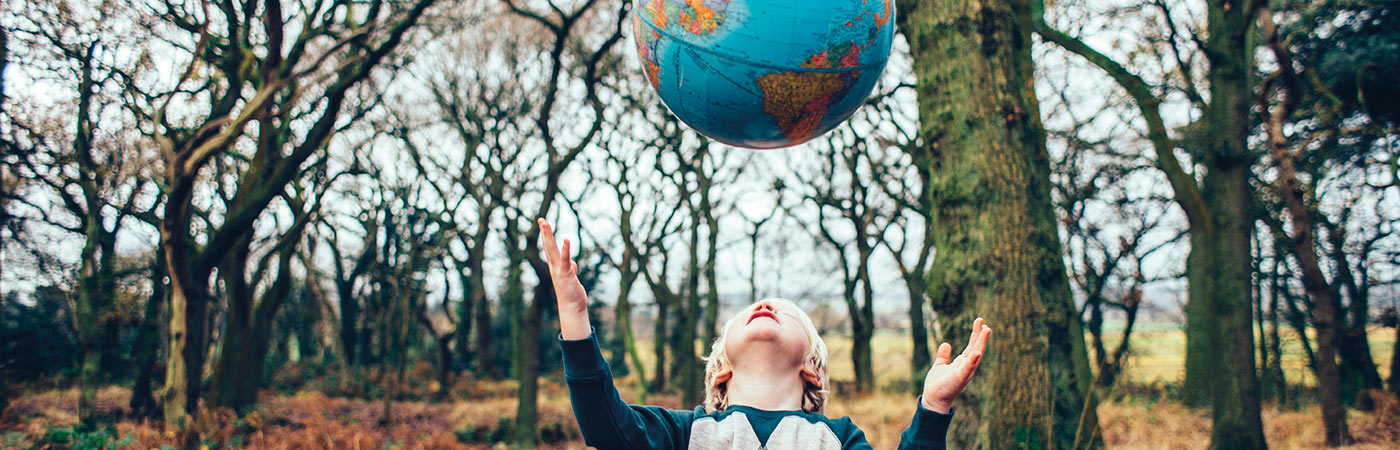 Young boy in forest throwing a world globe up to catch it