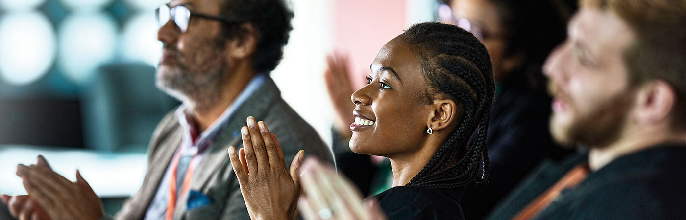 Seated rows of people, in smart workwear, smiling and clapping