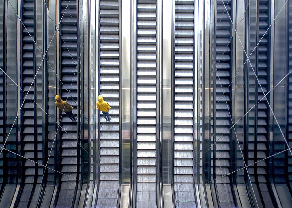 Woman wearing a yellow pullover standing on moving escalator