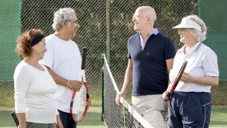 Four people smiling across a tennis court net.