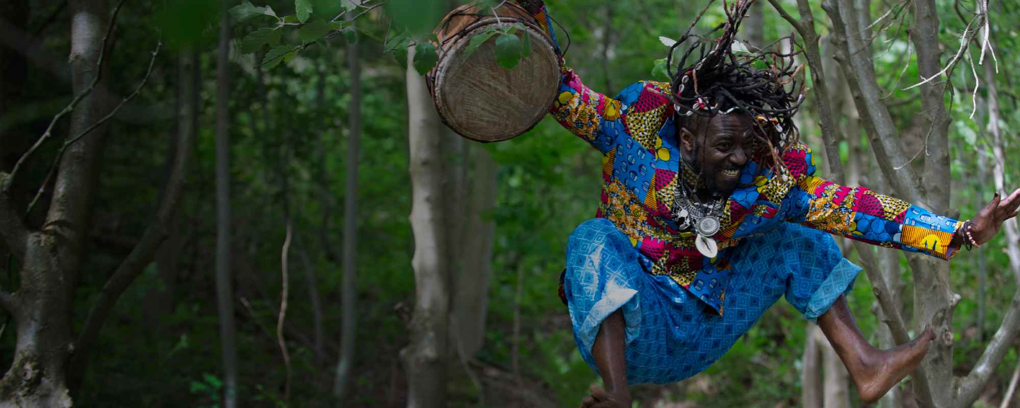 Man in woods jumping with drum