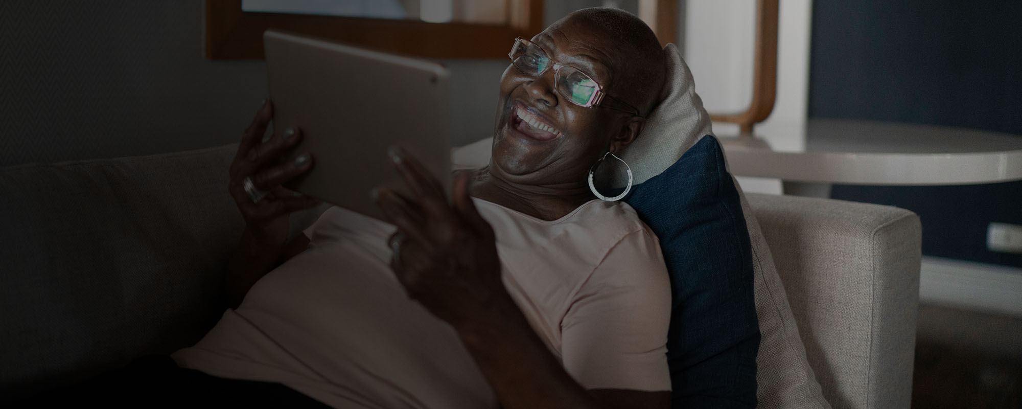 Woman reclining on couch laughing at something on her ipad