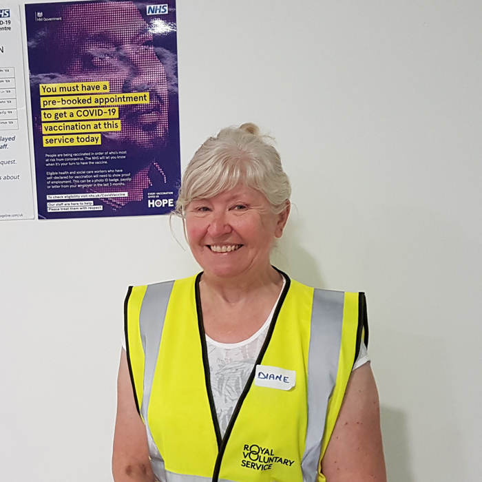 Diane standing in front of an NHS COVID poster